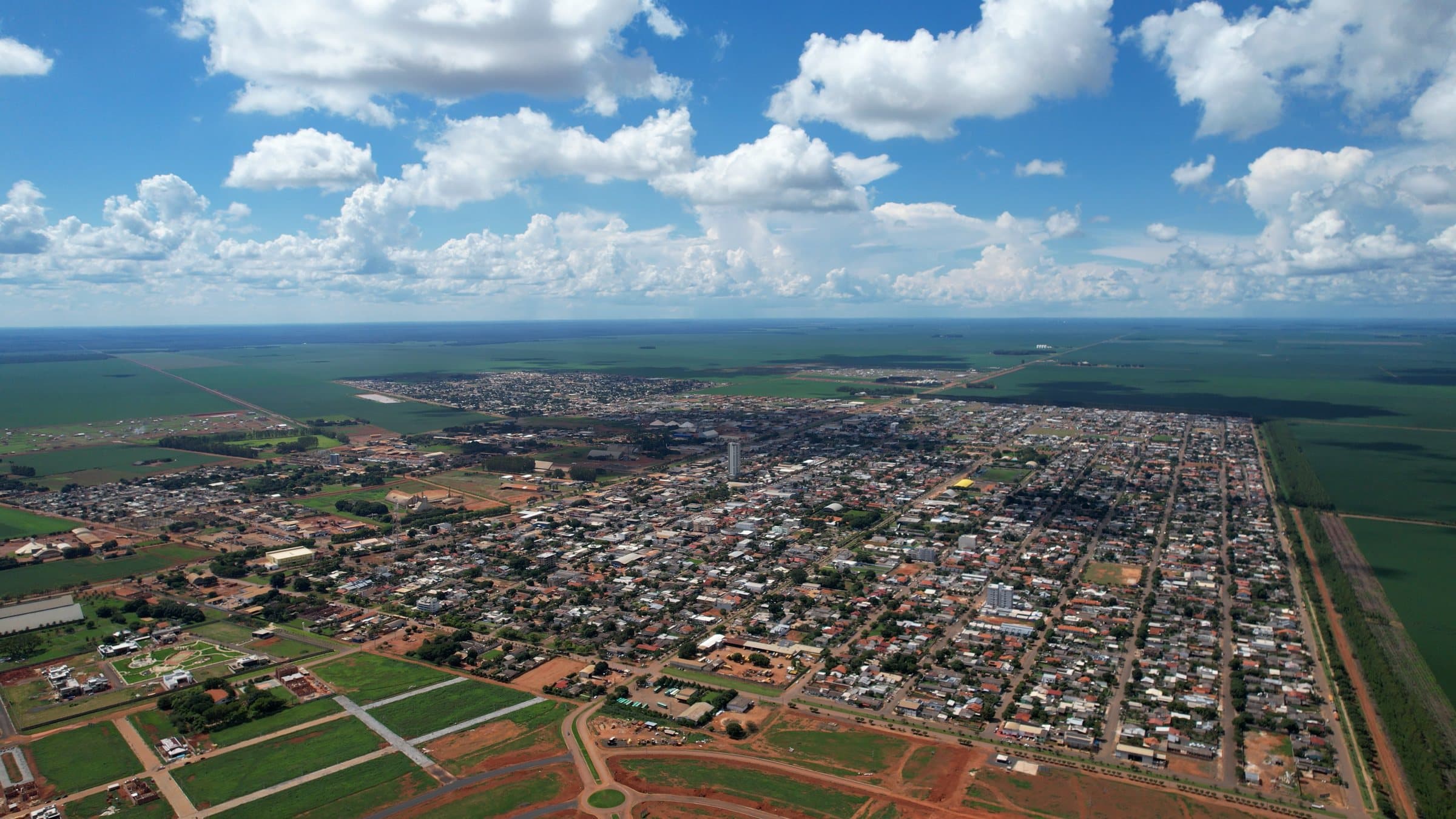 Vista aérea de Campo Novo do Parecis: a cidade em grade, a lavoura no horizonte e loteamentos novos sendo abertos em primeiro plano
