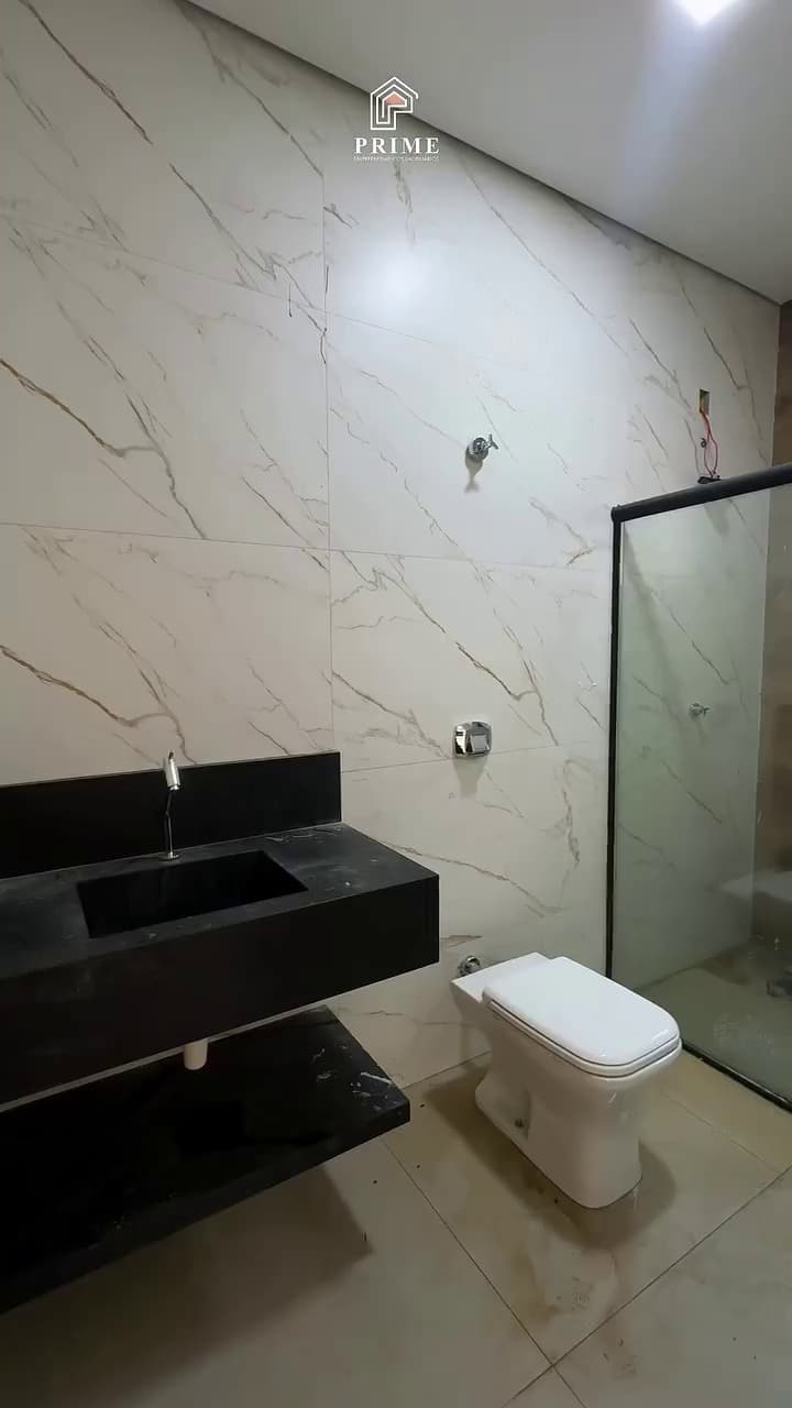 Banheiro com bancada escura, revestimento marmorizado até o teto e box de vidro