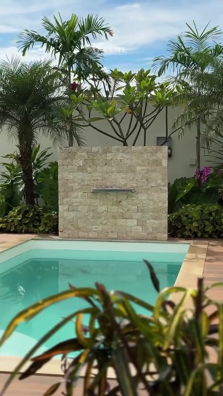 Piscina vista da área gourmet, com jardim e parede em pedra ao fundo