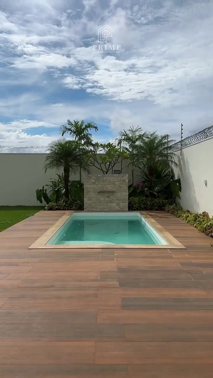 Piscina com deck em madeira, parede revestida em pedra e palmeiras